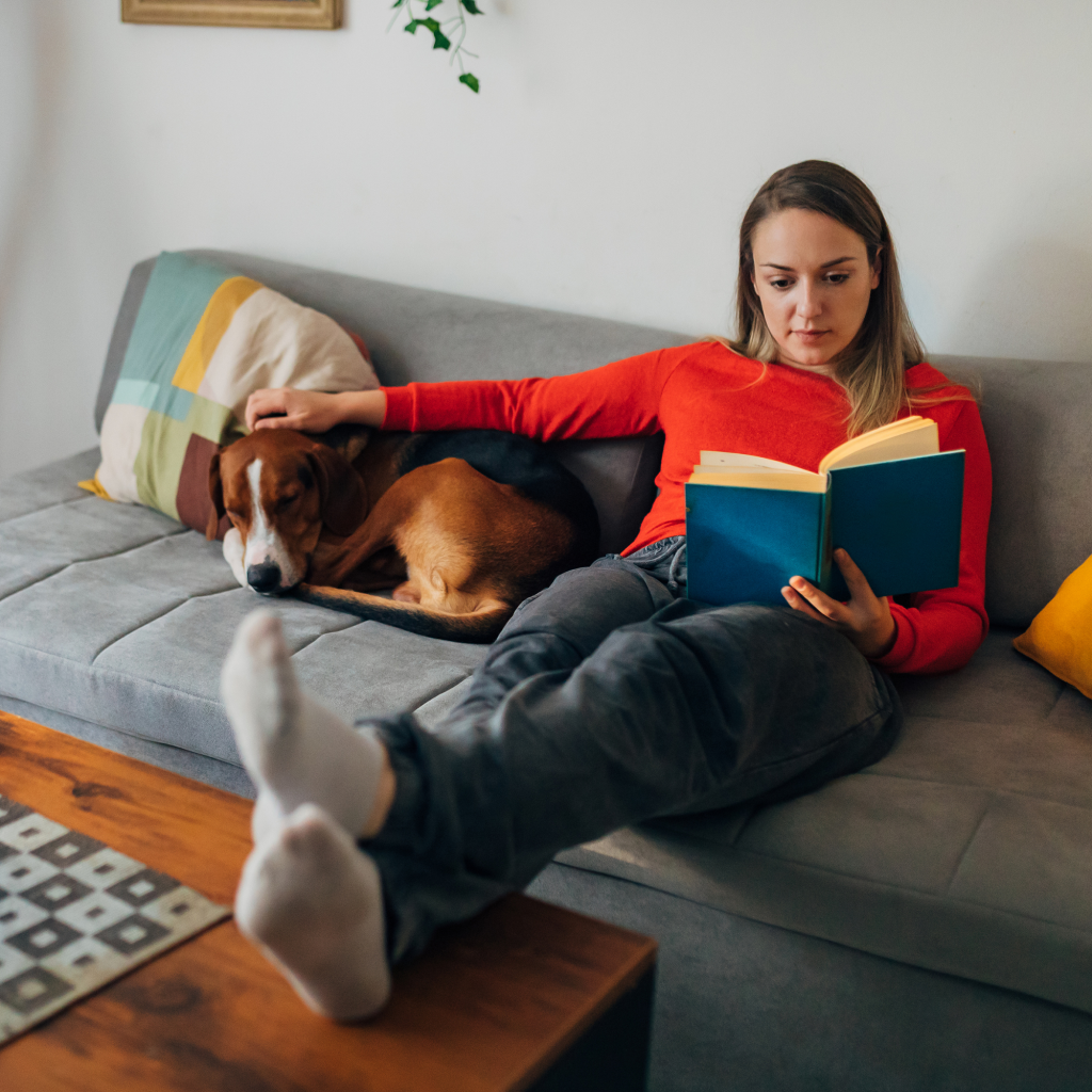 Woman reading a book, with dog lying next to her on sofa in living room