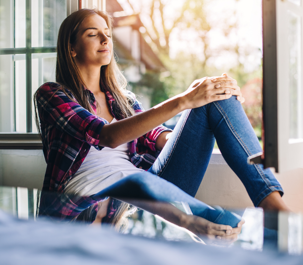 Young woman sitting at a windowsill having rest and fresh air