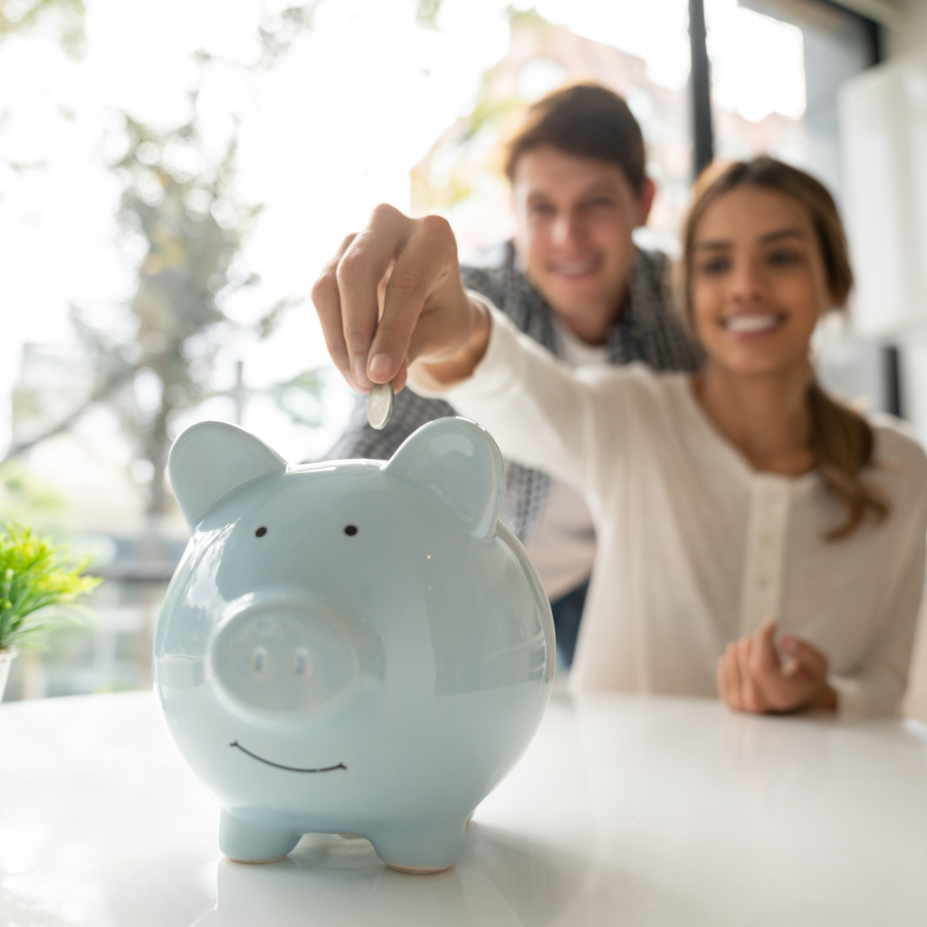 Focus on foreground of young couple saving coins into piggy bank