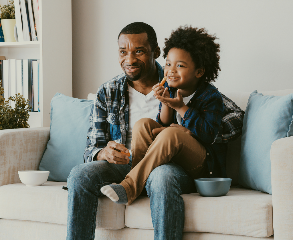 Dad and son sitting on a couch eating snacks